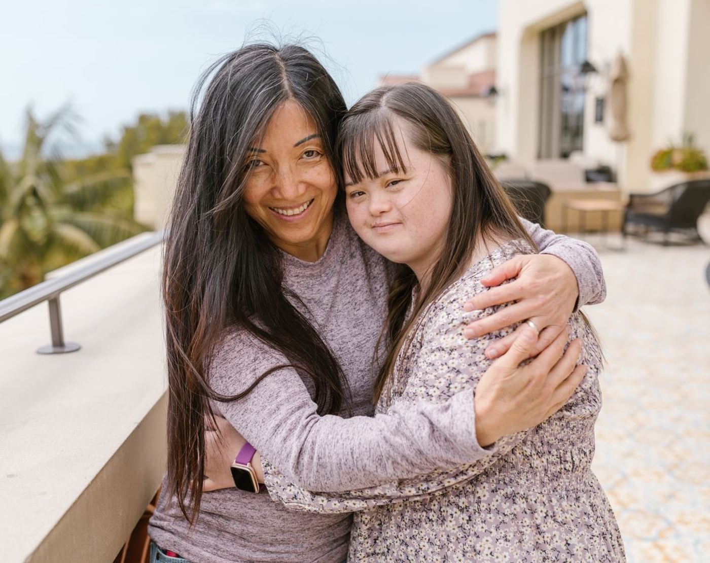 A mother and her teenage daughter hugging on a sunny patio